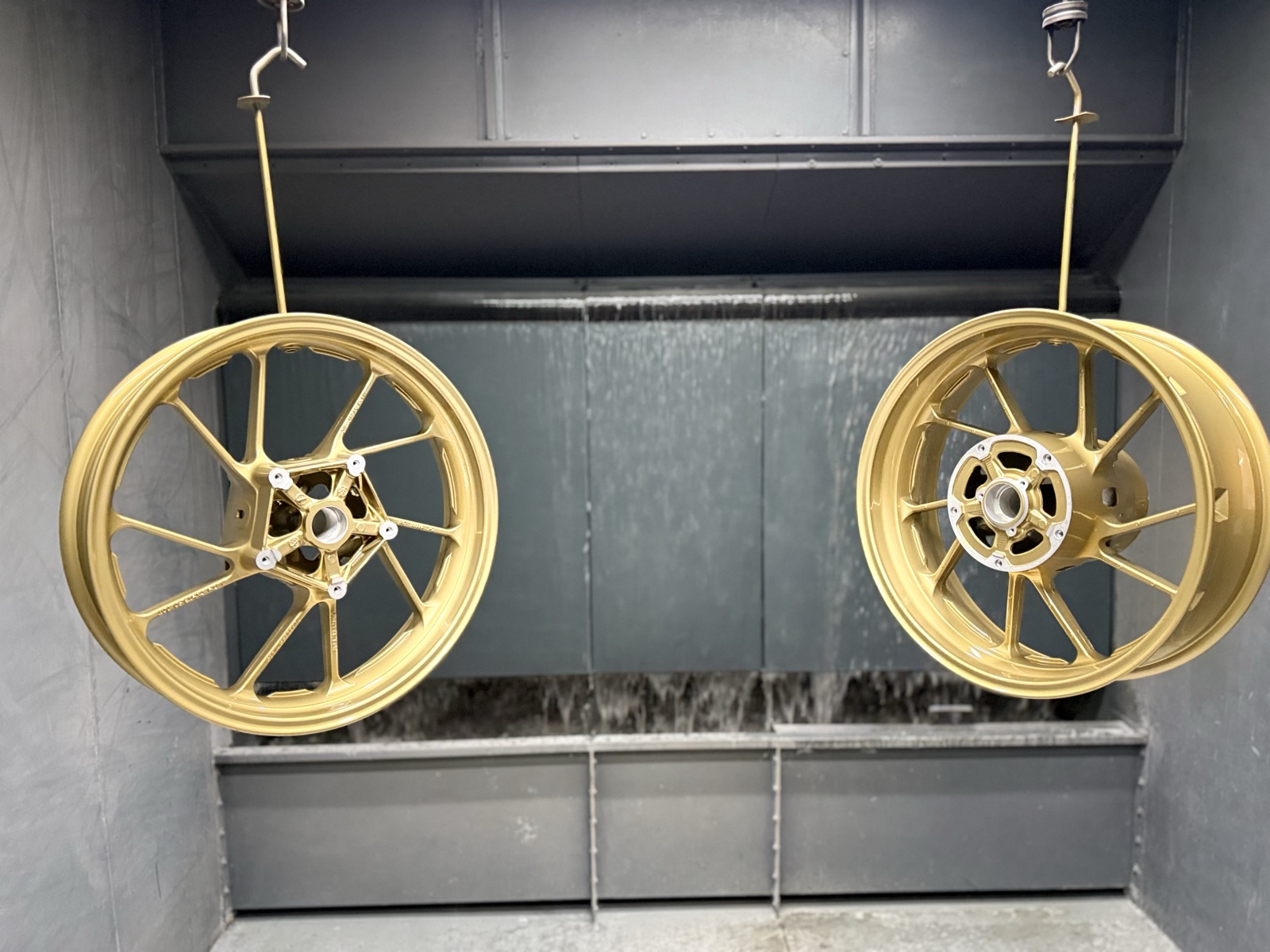 Gold powder coated motorbike wheels hanging in the spray booth